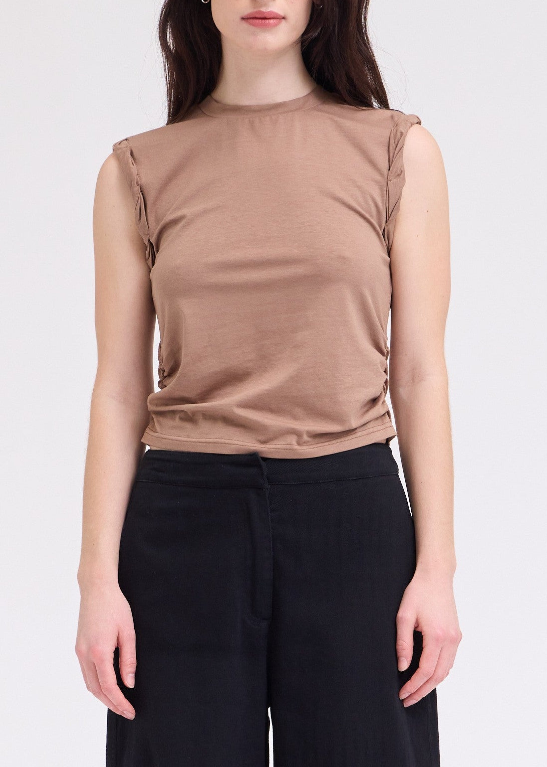 Woman wearing a brown sleeveless top and black pants on a white background