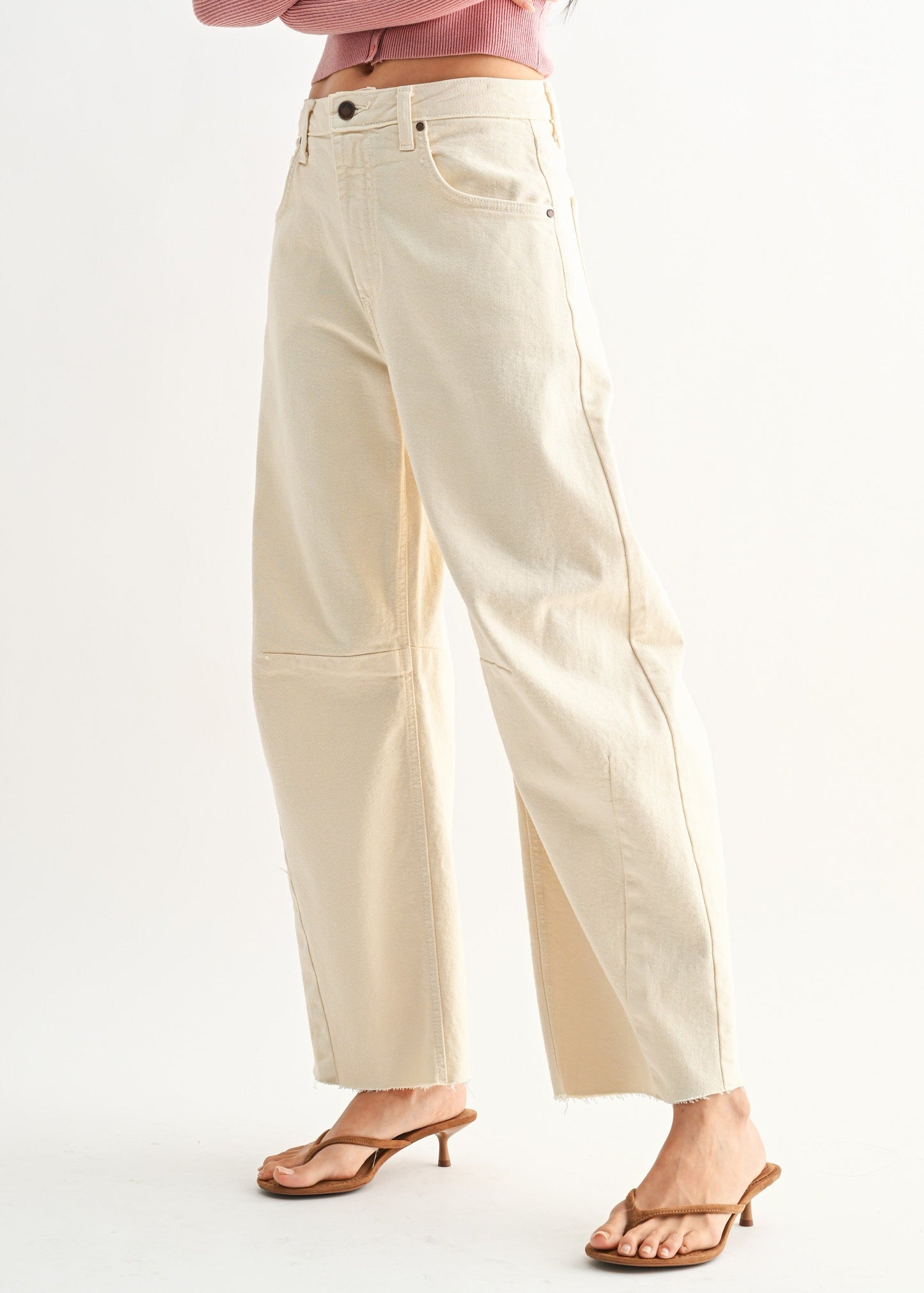 A woman modeling a dusty pink long-sleeve crop top and cream wide-leg pants with brown heeled sandals, standing against a plain white studio background.