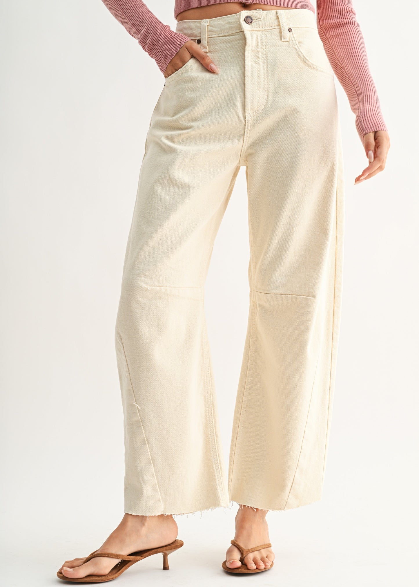A model wearing off-white wide-leg cropped jeans with patch pockets, styled with a pink ribbed long-sleeve top and brown heeled sandals against a clean white studio background.