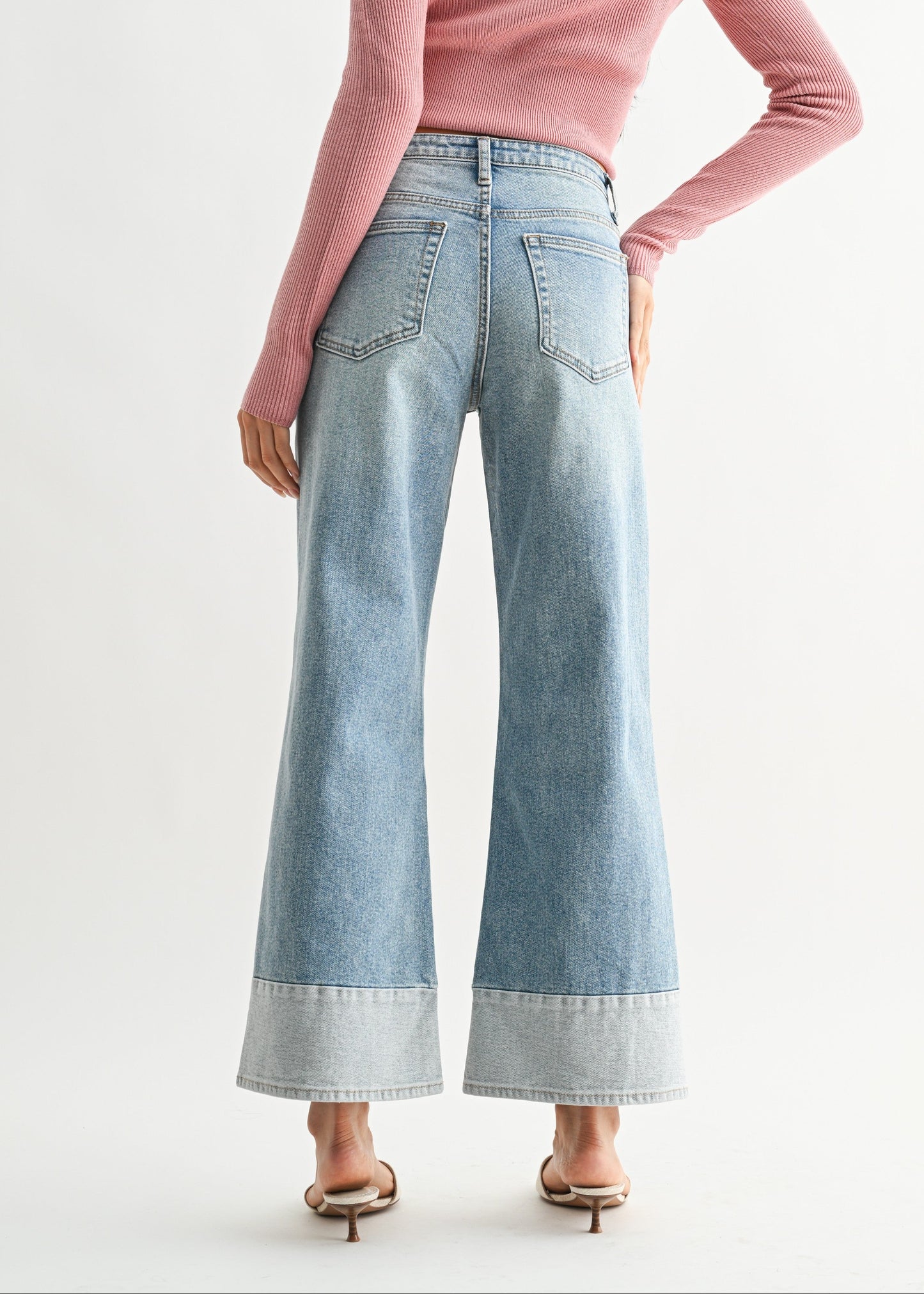 Woman wearing a pink sweater and light blue jeans on a white background