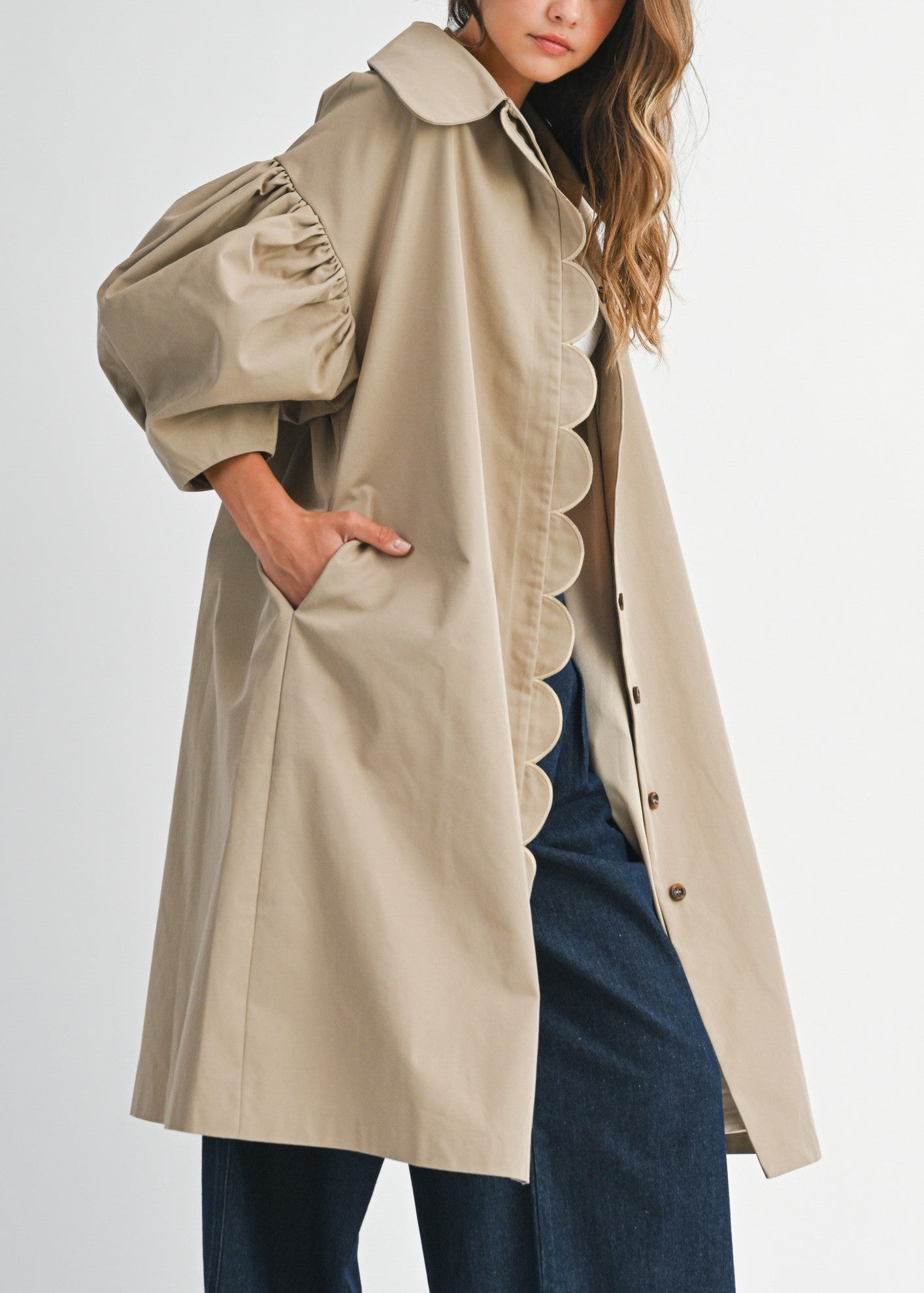 Woman wearing a beige trench coat with scalloped edges on a white background