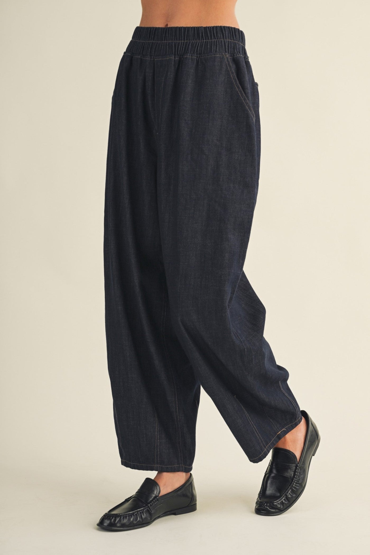 A person wearing dark navy wide-leg linen trousers and black loafers, shown from the waist down against a plain beige studio background.