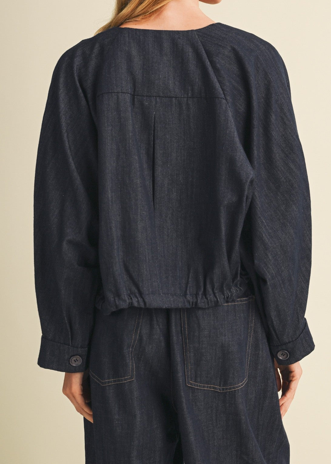 Person wearing a dark denim outfit on a beige background