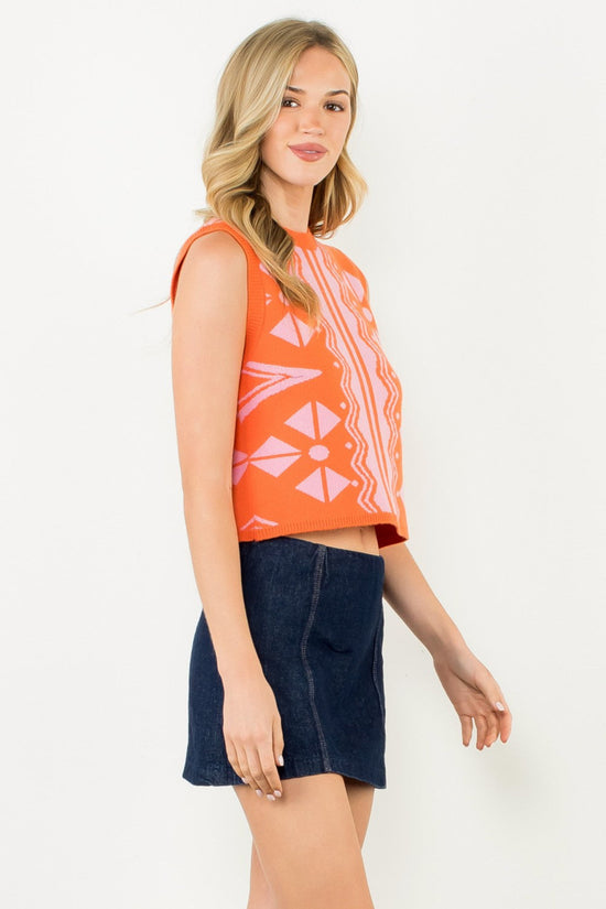 THML THML SLEEVELESS PATTERN KNIT TOP – ORANGE & PINK POP Woman wearing an orange sleeveless top with a floral pattern and a denim skirt on a white background